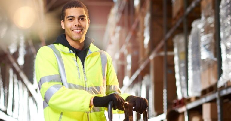 smiling warehouse worker with hands on hand truck